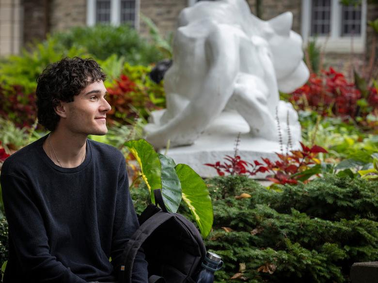 student gazing off into the distance with lion shrine behind him